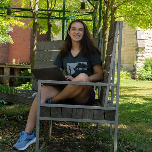 student sitting on a bench in the poetry garden with green foliage around